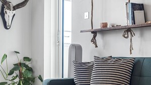 A room with a blue sofa, patterned pillows, a wall-mounted shelf with books and a skull, and a plant. - Modern 1 bedroom Apartment with views on West London - Pass the Keys (London)