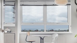 A room with a large window, a radiator, a table, two chairs, and a hanging light fixture. - Modern 1 bedroom Apartment with views on West London - Pass the Keys (London)