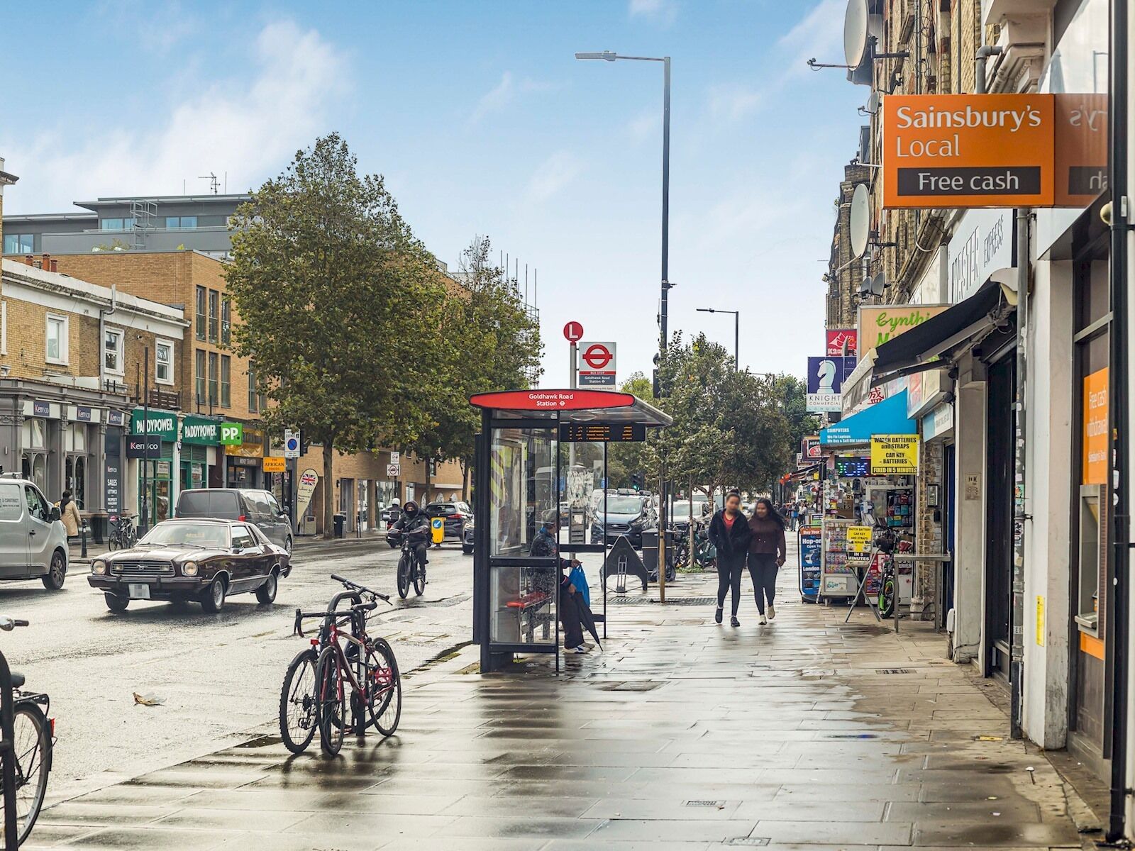 A street scene with a bus stop, shops, and pedestrians.