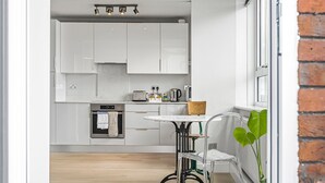 A modern kitchen with white cabinets, a built-in oven, a coffee maker, and a small dining table with a chair. - Modern 1 bedroom Apartment with views on West London - Pass the Keys (London)