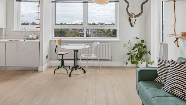 A modern kitchen with white cabinets, a dining table with chairs, a large window with a city view, and a green sofa with patterned cushions. - Modern 1 bedroom Apartment with views on West London - Pass the Keys (London)
