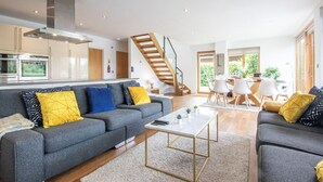 A modern living room with a grey sofa, a coffee table, and a staircase leading to another level. - Waters Edge 04, Waterside Lodge (P) - Lakeside Luxury House, Hot Tub, Sleeps 8 (Cirencester)