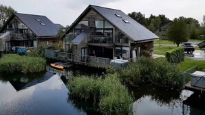 A modern house with a large balcony, a dock, and a boat. - Waters Edge 04, Waterside Lodge (P) - Lakeside Luxury House, Hot Tub, Sleeps 8 (Cirencester)