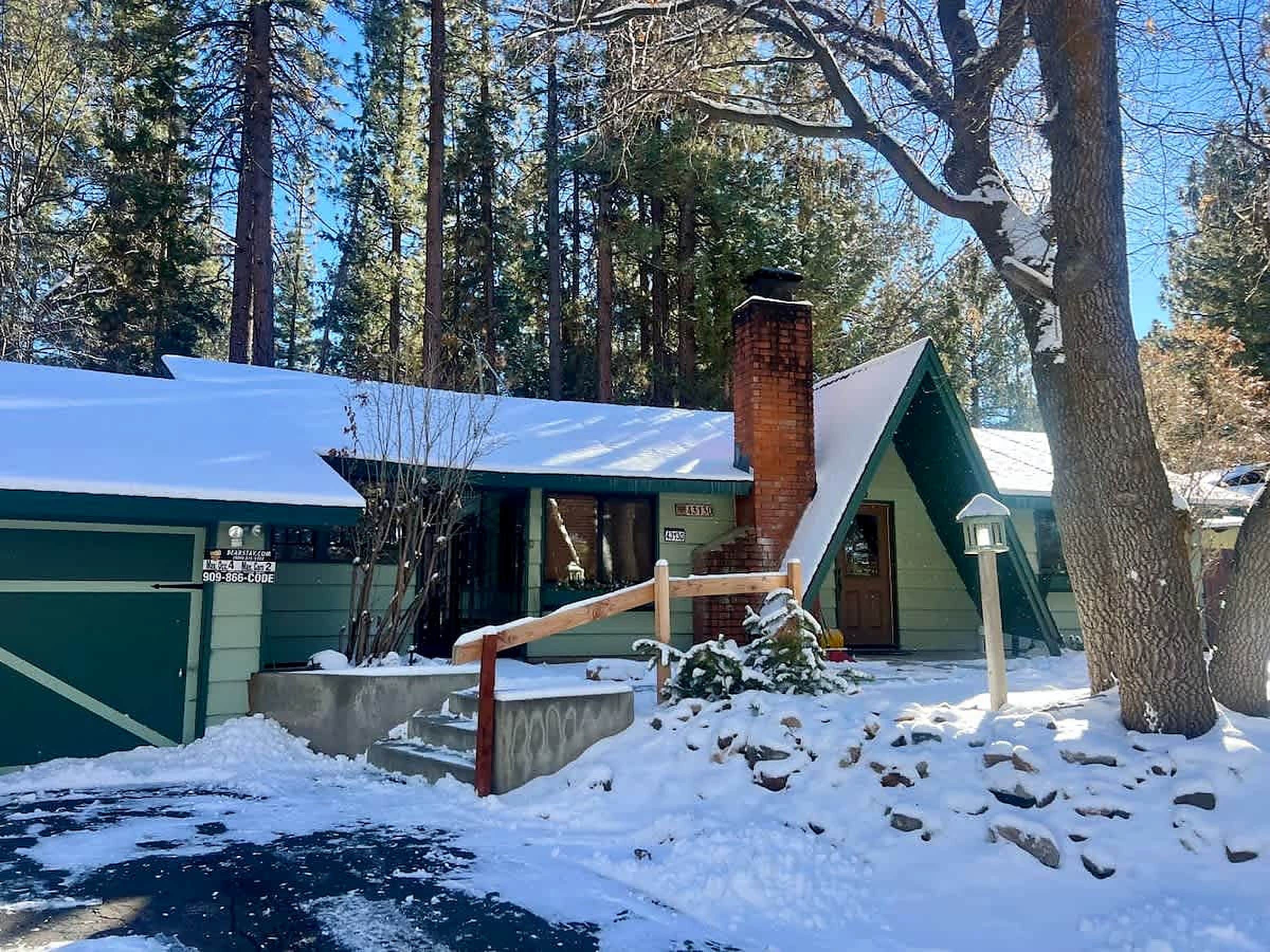 A cabin with a green exterior, a brick chimney, and a snow-covered roof.
