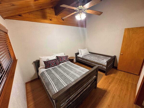 A bedroom with two wooden beds, a ceiling fan, and a wooden door. - Single-Story Cabin · Near Slopes · Fireplace & BBQ (Big Bear)