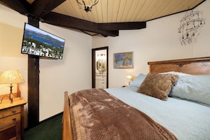 A bedroom with a bed, a television mounted on the wall, a wooden headboard, and a painting.