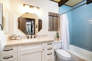 Un baño con tocador blanco, un espejo grande, inodoro y bañera con azulejos azules.