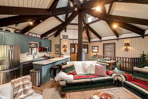 A spacious living area with a high ceiling, a cozy sofa set, a dining table, and a kitchen area with modern appliances. - Ski Cabin Steps to Snow Summit · Deck & BBQ (Big Bear)