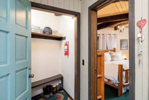 Una cama de madera en una habitación con una puerta azul, un extintor y un pequeño estante con objetos.