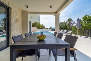 A modern outdoor dining area with a pool view, stone wall, and outdoor seating.