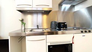Une cuisine compacte équipée d’une cuisinière en acier inoxydable, d’un four à micro-ondes et d’une machine à café.
