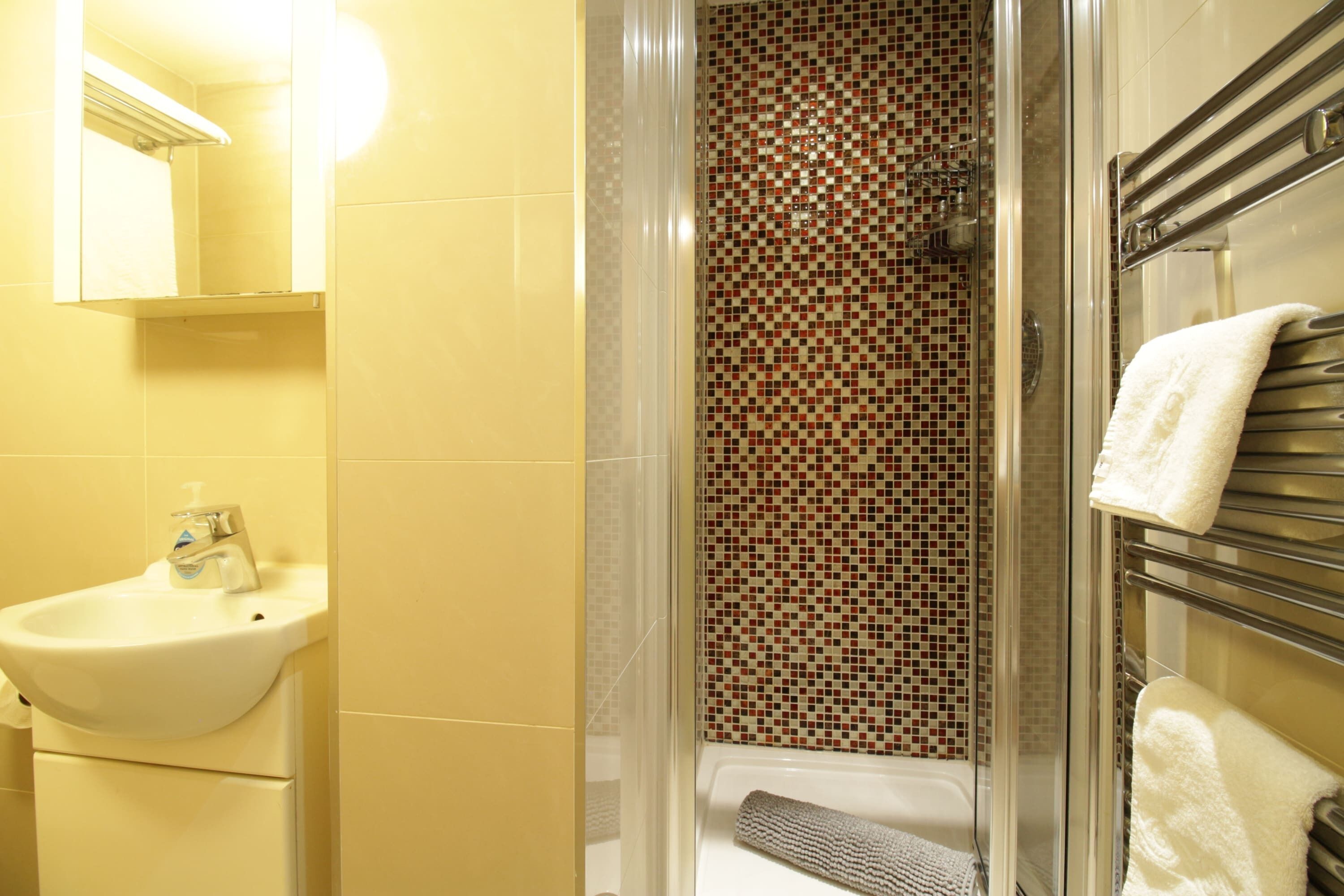 A bathroom with a sink, a shower with a tiled wall, and a towel rack.