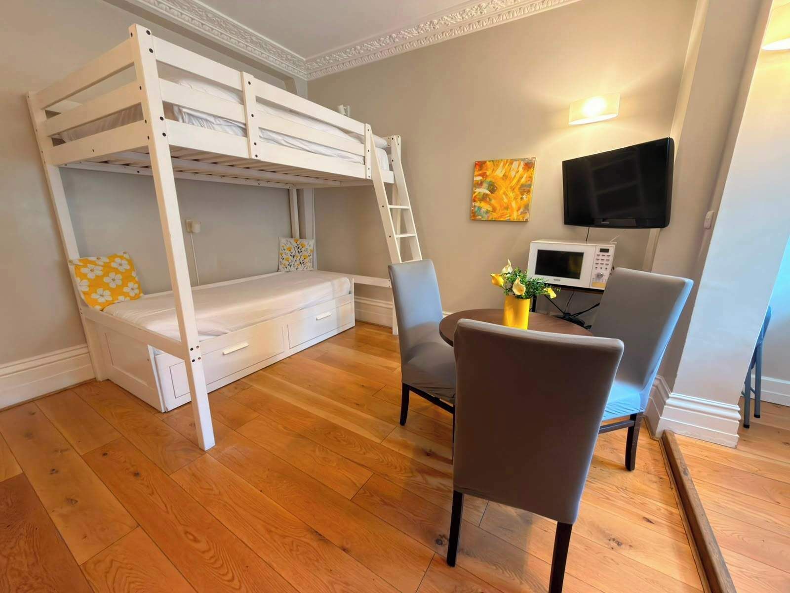 Een stapelbed met een bureau, een stoel, een televisie en een magnetron in een kamer met houten vloeren.