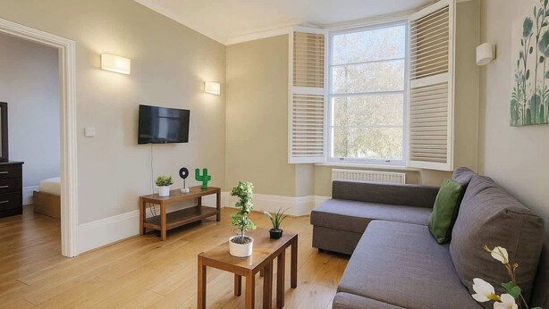 Een woonkamer met een grijze bank, een houten salontafel en een aan de muur bevestigde televisie.