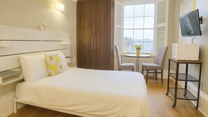 Ein Hotelzimmer mit Bett, Schreibtisch, Stuhl, Fernseher und einem Fenster mit Jalousien.