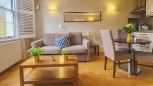 Een gezellige woonkamer met een bank, een bijzettafeltje en een eethoek met stoelen en een kleine tafel.