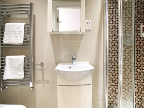 Een badkamer met een wit wastafelmeubel, een handdoekrek met twee handdoeken, een spiegel en een douche met mozaïektegels.