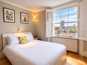 Een slaapkamer met een groot bed, een raam met luiken en twee ingelijste foto’s aan de muur.