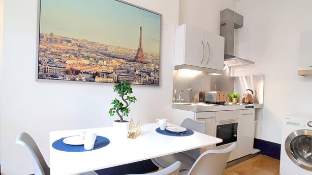 A modern kitchen with a view of a cityscape, a dining area with a table and chairs, and a washing machine. - S3 - Ground floor apartment by Marylebone (London)