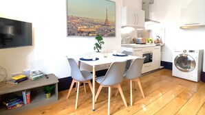 A modern kitchen with a washing machine, a dining area with a table and chairs, and a cityscape painting on the wall. - S3 - Ground floor apartment by Marylebone (London)