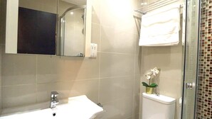 A bathroom with a white sink, a toilet, a glass shower enclosure, and a small potted orchid. - S3 - Ground floor apartment by Marylebone (London)
