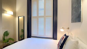 A hotel room with a large bed, a window with blinds, a bedside lamp, and a plant. - S3 - Ground floor apartment by Marylebone (London)
