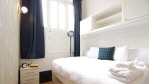 A bedroom with a bed, a bedside table with a lamp, a window with curtains, and a wall-mounted shelf. - S4 - Comfy Loft Apartment 10 Mins to Oxford Street (London)