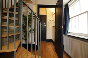 Un escalier avec des rampes en métal et des marches en bois, menant à une porte dotée d’un interrupteur et d’un thermostat fixé au mur.
