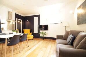 A modern living room with a grey sofa, a yellow armchair, and a dining area with a white table and black chairs.