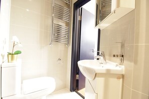 Un baño moderno con inodoro blanco, lavamanos y zona de ducha.