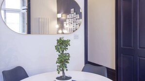A conference room with a round table, chairs, a potted plant, a large mirror, and a door. - S5 - Cute Apartment with Balcony by Oxford Street (London)
