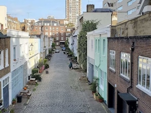Une rue pavée bordée de maisons à étages, dont certaines sont dotées de balcons et de plantes en pot.