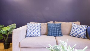 Un canapé beige agrémenté de coussins à motifs, placé devant un mur sombre et flanqué de deux lampes fixées au mur.