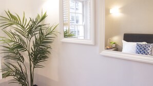 Une chambre avec un lit, une table de chevet, une lampe et une fenêtre avec des stores.