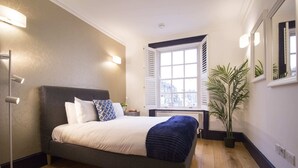 Une chambre à coucher avec un lit, une lampe de chevet, une fenêtre et une plante en pot.