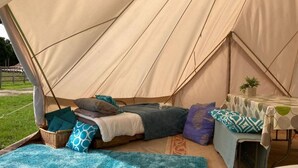 Ein Zelt mit einem Bett, Kissen, einem kleinen Tisch und einer Decke.