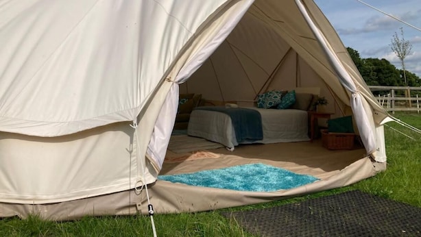 Ein großes, beiges Zelt mit einem Bett, einem kleinen Tisch und einem blauen Teppich auf dem Boden.