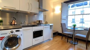 A compact kitchen with a washing machine, microwave, and a small dining area with a table and chairs. - S8 - Comfy Apartment in the heart of Hyde Park (London)