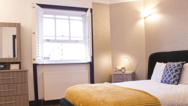 A bedroom with a bed, bedside table, lamp, and a window with blinds.