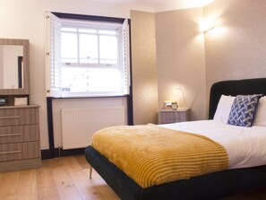 A bedroom with a bed, bedside table, lamp, and a window with blinds.