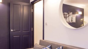 A room with a dark door, a round mirror on the wall, and a grey sofa with patterned cushions.