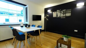 A modern room with a white table and blue chairs, a black wall with artwork, a TV, and a window with blinds.