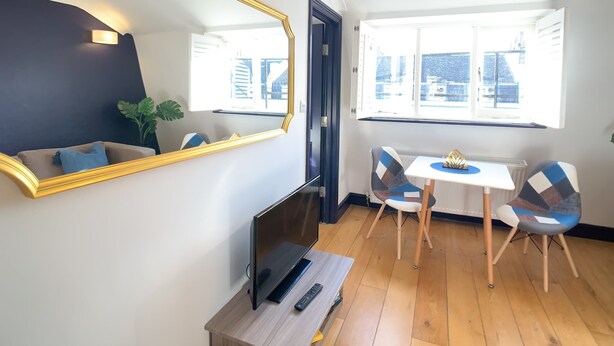 A modern living room with a large mirror, a flat-screen TV, a small table, two chairs, and a potted plant. - S11 - Attractive Penthouse in Paddington (London)