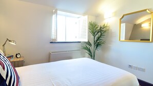 A bedroom with a bed, a nightstand with a lamp, a mirror, a window, and a radiator.