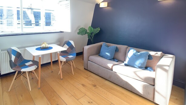 A modern living room with a beige sofa, a white table, and two chairs. There is a large window with a view of buildings.