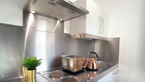 A compact kitchen with stainless steel appliances, including a stove, oven, and toaster, and a small potted plant on the counter.
