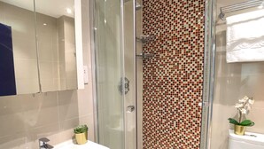 A modern bathroom with a glass shower enclosure, a white sink, and a tiled wall with a mosaic pattern.
