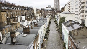 A narrow cobblestone street lined with terraced houses, featuring satellite dishes and a mix of residential and commercial buildings.