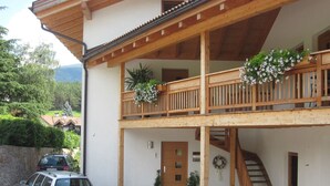 A two-story building with a wooden balcony, a stone-paved entrance, and a car parked in front. - Ferienwohnung mit Schwimmbad (Schabs)