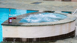 A hot tub with two glasses of red wine and a bottle, surrounded by a stone pool. - Ferienwohnung mit Schwimmbad (Schabs)